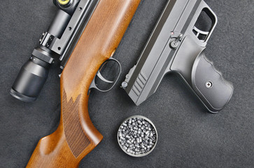 Wooden air gun and pistol with pellets on black background
