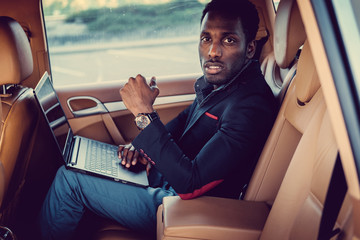 African man in a suit using laptop in a car.