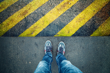 Industrial striped asphalt road warning yellow black pattern with person legs.
