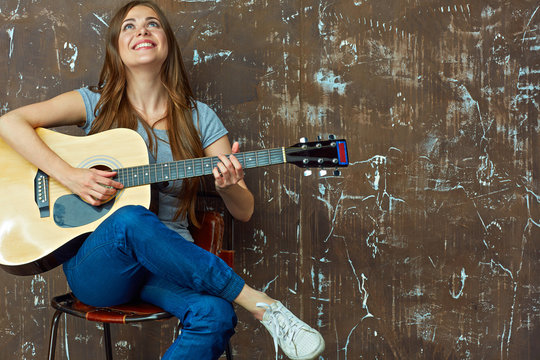 Young woman sitting with guitar on grunge wall background.