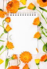 Notebook with flowers marigold on wooden background.