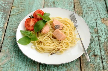 Pasta with tomatoes, green basil and salmon filet in white plate
