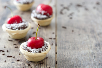Delicious chocolate tartlets with one cherry and coconut on a wooden table

