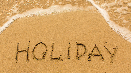 Holiday - inscription on sand beach with the soft wave.