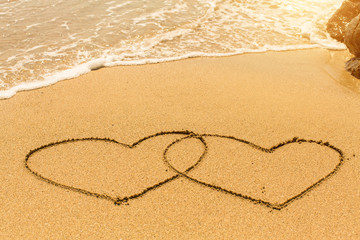Obraz na płótnie Canvas A pair of hearts drawn on sand beach with the soft wave.