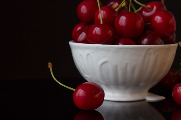 Cherry in white plate on black background.
