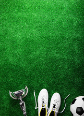 Soccer ball, cleats and trophy against green artificial turf