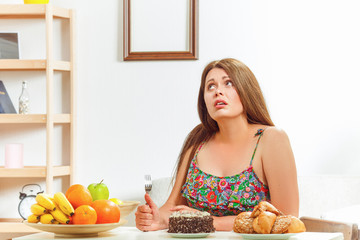 Portrait of fat woman on diet sitting at table with spoon in her hand and thinking whether to eat...