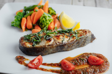 Baked fish with lemon, ketchup and tomato on white plate