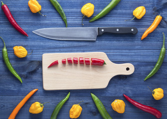 chopped cayenne chilli pepper on cutting board with knife and cayenne chilli peppers and habanero peppers on blue wooden table. Image with copyspace.