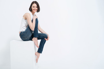 Beautiful young woman sitting on white cube in studio
