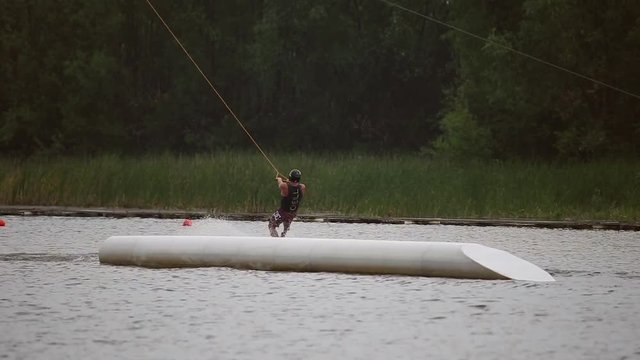 Athlete wakeboarder jumping on trampolines in wakeboarding park on the lake

