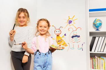 Two happy girls drawing funny picture at the wall
