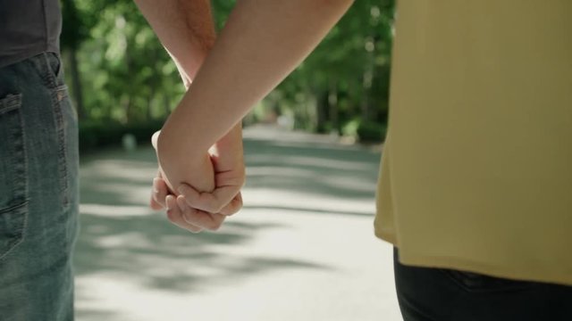 Young couple walking hand to hand in the park. Close up. Dolly shot.