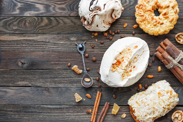 Rustic wooden background with different pastries - chocolate and peanut meringue, tart, marzipan bun. Different spices - cinnamon, walnuts, peanuts, ginger. Top view of tasty desserts. Place for text.