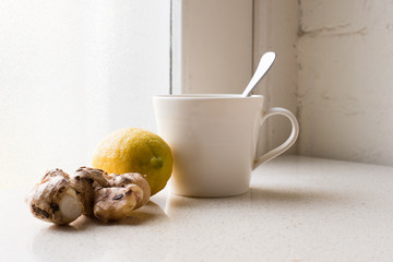 Ginger and lemon next to white cup on white table against window and rustic white brick wall (selective focus)