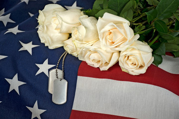 Military dog tags and white rose bouquet on American flag.