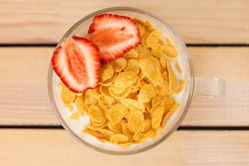 cornflakes with milk and strawberries for breakfast, on a wooden background