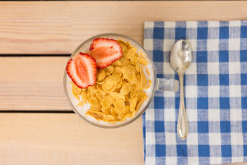 cornflakes with milk and strawberries for breakfast, on a wooden background