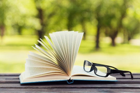 Open book and eyeglasses on a bench in park in a sunny day, reading in the summer, education, textbook, back to school concept