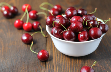 Sweet cherries in the white bowl on the wooden table.