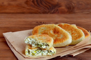 Fried pies stuffed with cheese, green onion and dill. Delicious homemade pies on paper and wooden background. Food idea for a summer picnic