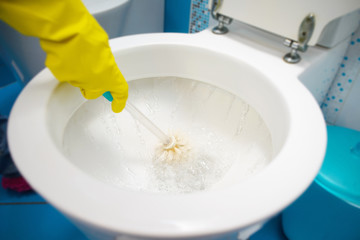 A woman cleans a bathroom toilet with a scrub brush.