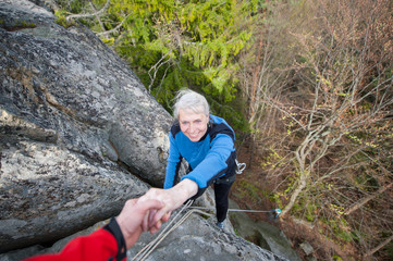 Male rockclimber is helping a climber female to reach a peak of mountain. Man giving a hand to the...