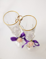 Two glasses with violet bands and roses, and wedding rings on it