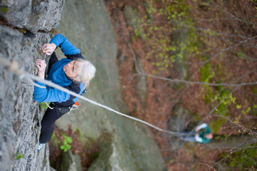 Woman practices in climbing at the rock in the mountains. Another man belay on the ground. Close-up view from above