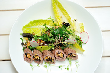 image of salad with lamb, prunes and sheep cheese. 
On a white plate horizontally