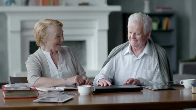 Happy elderly man and woman using computer. They close it and look at each other