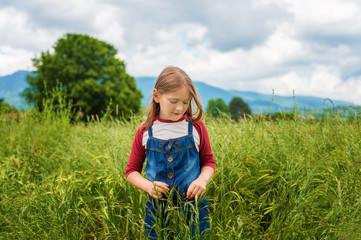 Little girl playing in green wheat field in summertime, wearing red and white t-shirt and overalls