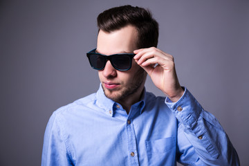 portrait of young handsome man in sunglasses over gray