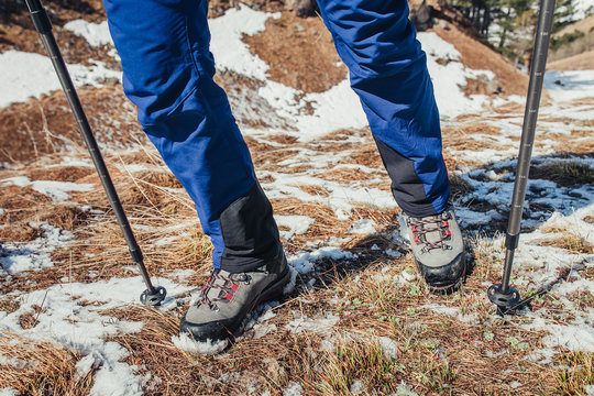 Close-up of hiking boots and poles sticks on the snow covered grass in early spring in the mountains