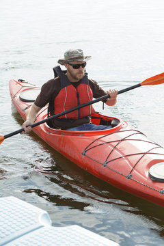 Man boating in red canoe in river at summer day