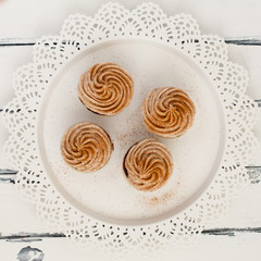 fyra stycken cupcake med spritsad topping på vitt fat mot vit trä bakgrund