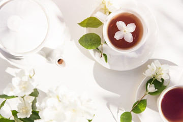 Top view on cup of tea with jasmine flower and vase of jasmine flowers on the garden table.