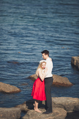 Romantic loving couple posing on stones near sea, blue sky