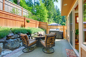 Backyard patio area with table set and concrete floor.