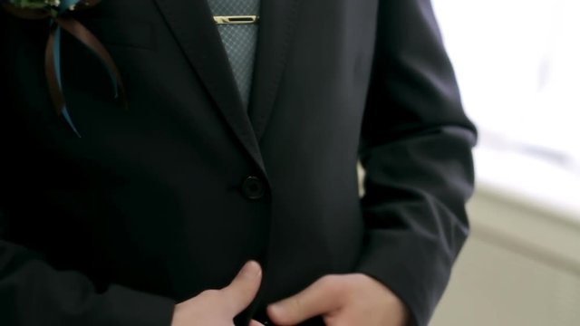 Young groom buttons his jacket in front of a mirror