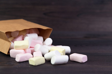 Fototapeta na wymiar White and pink marshmallows spill out of the package on the dark wooden background