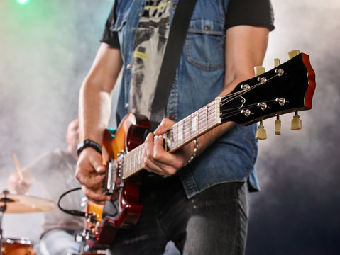 Rock band performs on stage. Guitarist and drums.