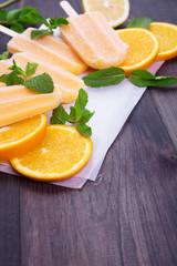 Frosty popsicles on a paper with mint and oranges on a dark wooden background