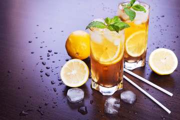 Two glasses of iced tea with lemon and mint on a dark wooden background