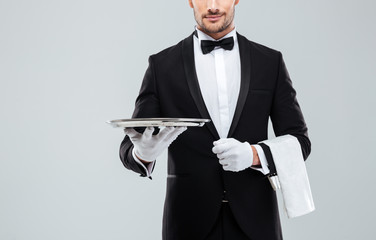Waiter in tuxedo holding metal empty tray and napkin