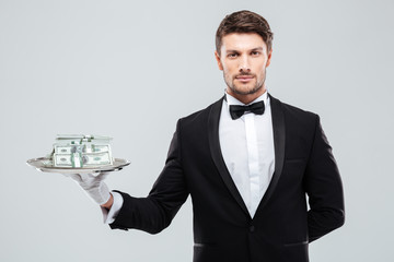 Handsome waiter in tuxedo standing and holding money on tray