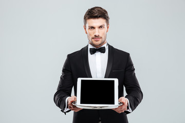 Butler in tuxedo holding blank screen tablet on tray