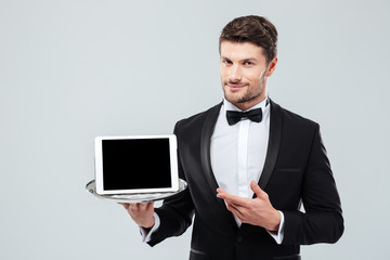 Butler in tuxedo holding and pointing at blank screen tablet