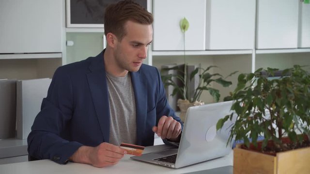 Successful Business Guy Ordering Ticket On Sport Game Or Buying Flowers Via Internet. Ceo In Big Company Entry Number Of Security Code From Debit Card On Computer. Smiling Businessman Enjoy His